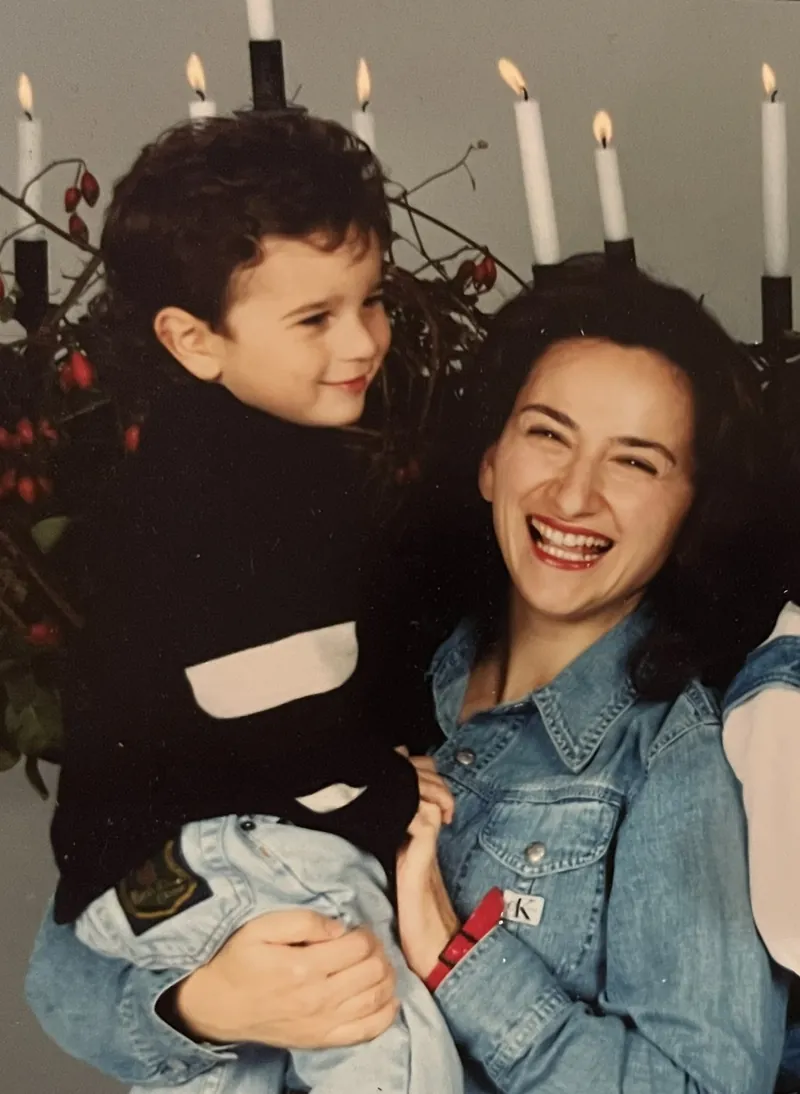 Lina, laughing, holding her young son in front of a row of lit candles.